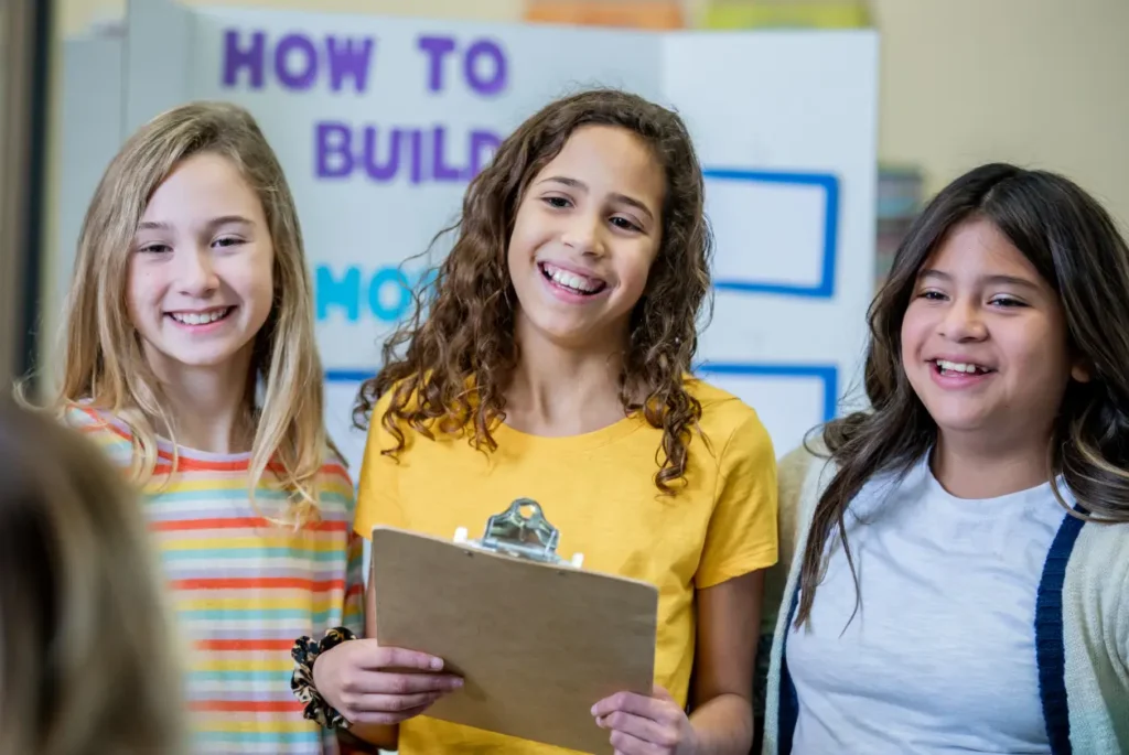 Student holding a clipboard with 2 girls at a science fair